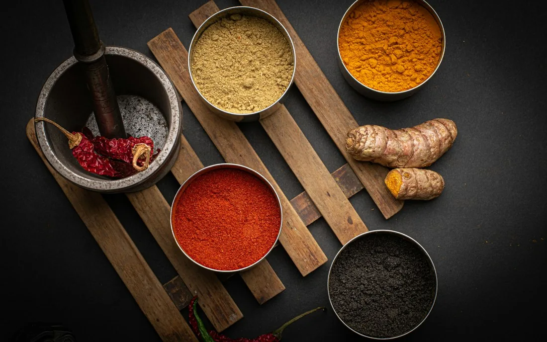 Bowls of turmeric, red chilli and other ground spices with fresh turmeric root