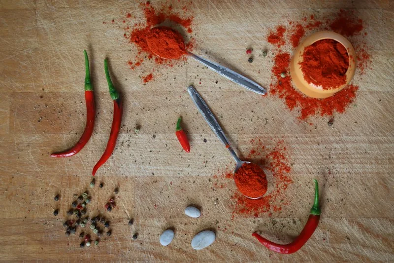 Spoons of ground spice with red chillies on a wooden board