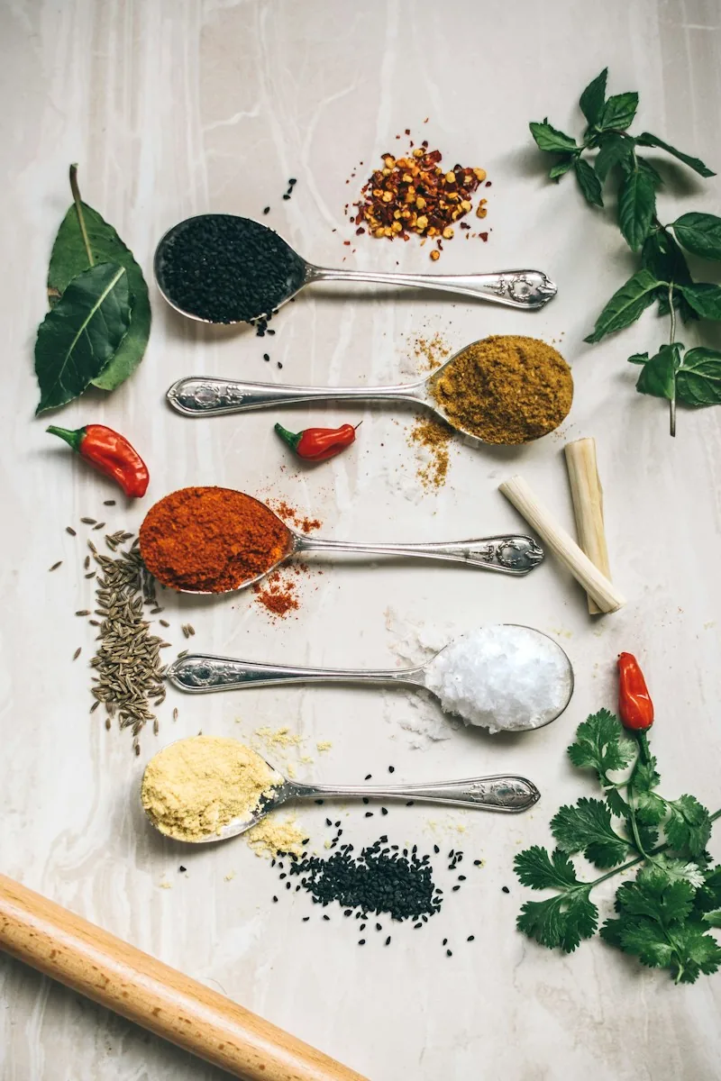 Spoons of assorted whole and ground spices with fresh herbs
