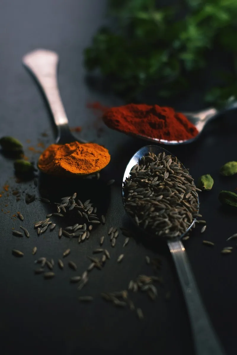 Spoons of cumin seeds and ground spices on a dark surface